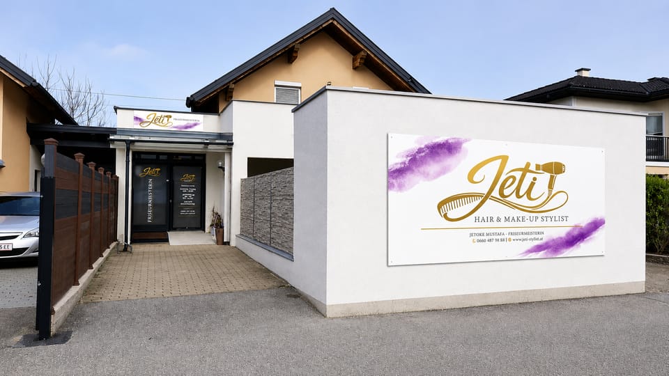 Außenansicht des Salons Jeti in Schalchen mit großer Wandbeschriftung „Jeti — Hair & Make-Up Stylist“ und Eingang.